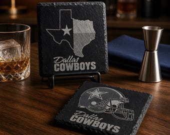 May include: Black slate coasters with the Dallas Cowboys logo and team name. One coaster features the Texas state outline with a star, and the other displays a football helmet. The coasters are on a dark wooden surface.