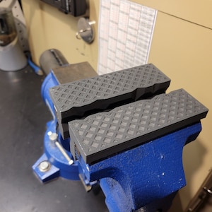 May include: Two black rubber pads with a diamond pattern are clamped in a blue metal vise.