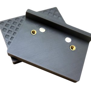May include: A gray 3D printed adapter plate with two gold screws and two white circles. The plate has a textured surface.
