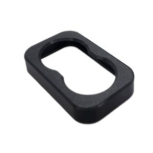 May include: A black, rectangular object with rounded corners and a central cutout. The object has a textured surface and appears to be made of a solid material. The shape is reminiscent of a frame or a holder.