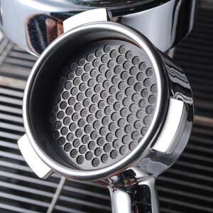 May include: A close-up of a silver espresso portafilter with a black, honeycomb-shaped filter basket.