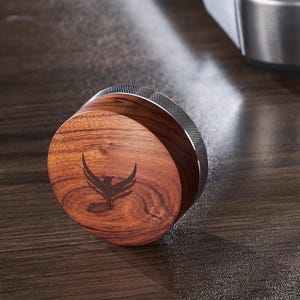 May include: A round wooden tamper with a silver metal band. The tamper has a bird logo engraved on the top.