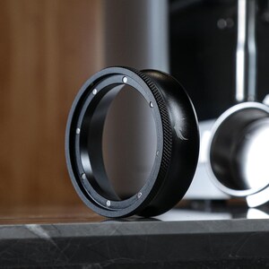 May include: A black metal ring with a textured outer edge and a smooth inner edge. The ring has a small, silver logo on the side.