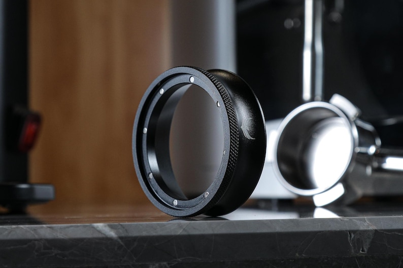 May include: A black metal ring with a textured outer edge and a smooth inner edge. The ring has a small, silver logo on the side.