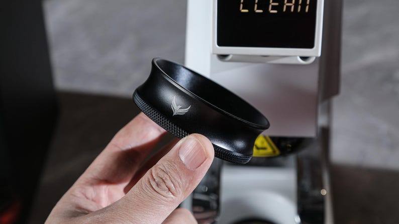 May include: A black metal portafilter with a silver logo, held in a hand.