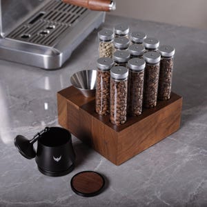May include: A wooden stand with glass tubes filled with coffee beans. The stand has a stainless steel funnel and a black coffee grinder with a lid.