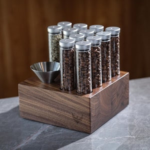 May include: A wooden stand with a silver funnel and 12 glass tubes filled with coffee beans. The stand has a logo of a bird with wings spread.