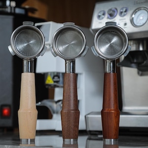 May include: Three espresso portafilters with wooden handles. The handles are made of different types of wood: light wood, dark wood, and reddish wood.