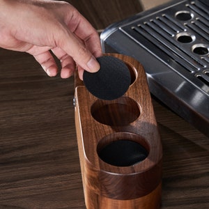 May include: A wooden coffee pod holder with three compartments, each lined with black felt. The holder is made of dark wood and has a rounded shape.