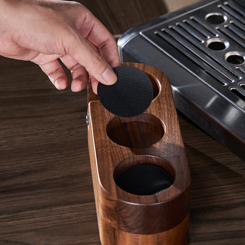 May include: A wooden coffee pod holder with three compartments, each lined with black felt. The holder is made of dark wood and has a rounded shape.