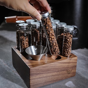 May include: A wooden stand with eight glass tubes filled with coffee beans. The stand has a funnel in the center and a black surface.