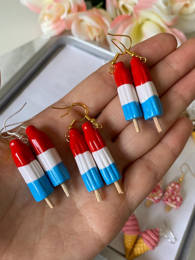 Puede incluir: Pendientes artesanales con dise&ntilde;o de helado de paleta en rojo, blanco y azul. Cada pendiente presenta un dise&ntilde;o de mini helado de paleta con un palito de madera y ganchos dorados. Un divertido accesorio veraniego.