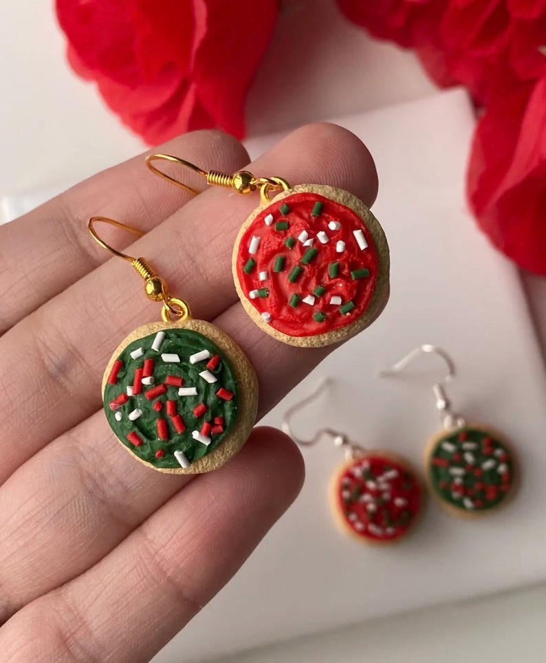May include: Cookie-shaped earrings with gold-coloured hooks. One earring has red icing with white and green sprinkles, the other has green icing with red and white sprinkles. A festive accessory.