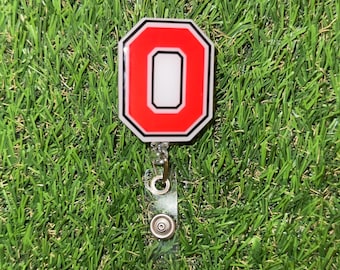 May include: A red and white letter "O" badge holder with a clear plastic strap and silver metal clips.