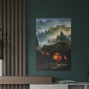 May include: A canvas print depicting a fantasy village nestled in a misty mountain landscape. The artwork features cozy hobbit-hole-like homes with glowing windows and thatched roofs, evoking a sense of warmth and tranquility. The color palette includes greens, browns, and warm yellows.