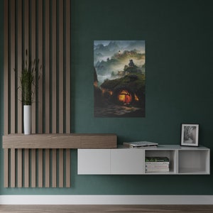May include: A canvas print depicting a fantasy landscape with hobbit-style homes nestled into a hillside. The artwork features warm interior lighting, a stone path, and a misty mountain backdrop. The color palette includes greens, browns, and warm orange hues.