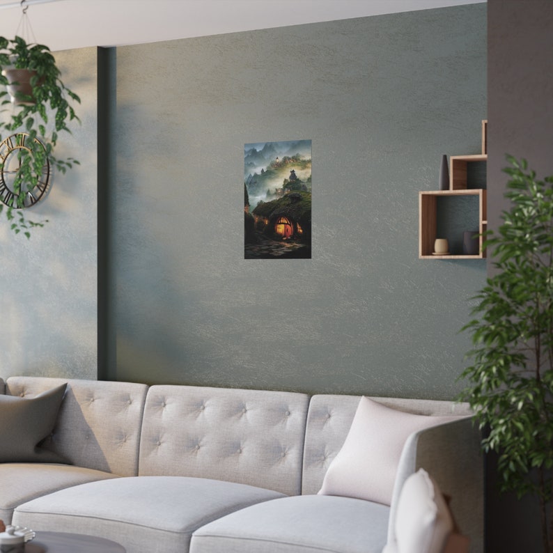 May include: A vertical art print depicting a fantasy landscape with a hobbit-hole style dwelling. The artwork features a warm, inviting glow emanating from the doorway, set against a backdrop of misty mountains and a cloudy sky. The print is displayed on a wall.