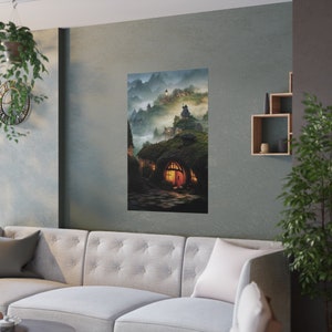 May include: A vertical poster featuring a fantasy landscape with hobbit-style homes nestled into a hillside. The artwork depicts a village with glowing windows, a winding stone path, and misty mountains in the background. The color palette is dominated by greens, browns, and blues.