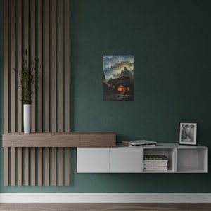 May include: A framed art print depicts a fantasy landscape with a hobbit-hole style dwelling. The artwork features a warm, inviting glow emanating from the windows of the home, set against a backdrop of misty mountains and a twilight sky. The print is displayed on a teal wall.