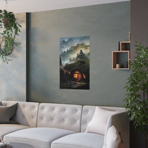 May include: A vertical art print depicting a fantasy village nestled in a misty mountain landscape. The artwork features cozy, illuminated hobbit-style homes with arched doorways and a winding stone path. The color palette includes greens, browns, and warm orange hues.