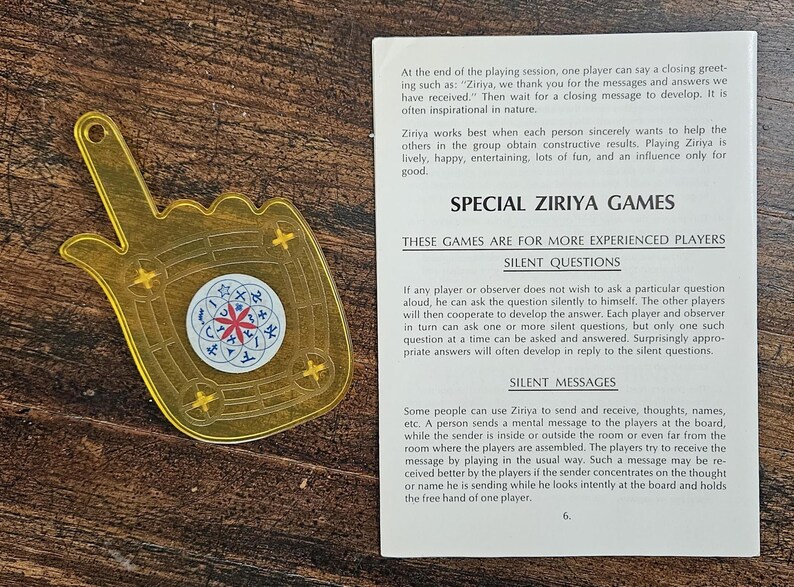 May include: A golden-yellow Ziriya game piece shaped like a hand, featuring a circular emblem with a red star design. Text on a page details the game's rules and features.
