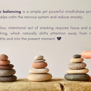 May include: Three stacks of smooth, rounded river stones in shades of gray, tan, and reddish-brown. The text reads: Stone balancing is a simple yet powerful mindfulness practice that helps calm the nervous system and reduce anxiety. The slow, intentional act of stacking requires focus and steady breathing, which naturally shifts attention away from racing thoughts and into the present moment.