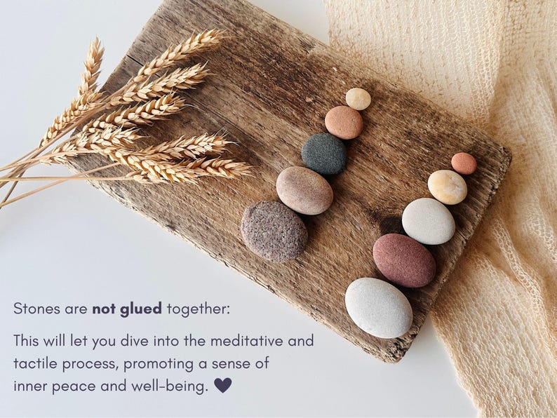 May include: Two vertical stacks of smooth, multi-colored river stones arranged on a weathered wooden board, accompanied by dried wheat stalks. The text reads: Stones are not glued together: This will let you dive into the meditative and tactile process, promoting a sense of inner peace and well-being.