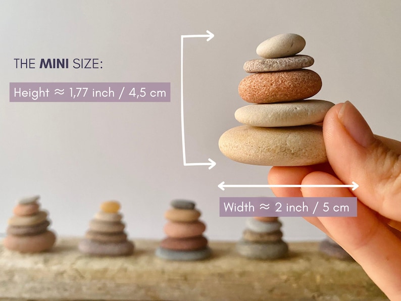 May include: A stack of five smooth, rounded, multi-colored pebbles. Text reads THE MINI SIZE: Height 1.77 inch, Width 2 inch. The stack is held, with four additional pebble stacks visible in the background on a textured, light-colored surface.
