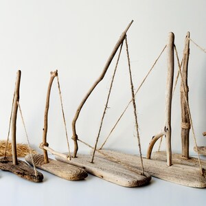 Puede incluir: Una colecci&oacute;n de veleros artesanales de madera flotante. Cada barco presenta una base de madera, un m&aacute;stil hecho de ramas y aparejos de cuerda. Los tonos naturales de la madera y el dise&ntilde;o simple crean una est&eacute;tica r&uacute;stica y n&aacute;utica.