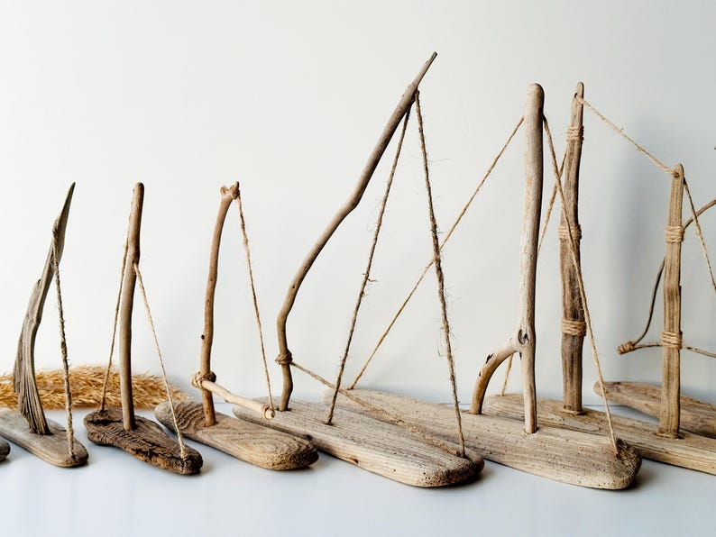 Puede incluir: Una colecci&oacute;n de veleros artesanales de madera flotante. Cada barco presenta una base de madera, un m&aacute;stil hecho de ramas y aparejos de cuerda. Los tonos naturales de la madera y el dise&ntilde;o simple crean una est&eacute;tica r&uacute;stica y n&aacute;utica.