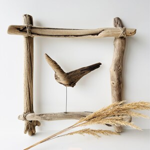 May include: A rustic wooden frame with a driftwood sculpture and dried wheat stalks. The frame is constructed from weathered wood pieces tied together with twine. The sculpture resembles a bird in flight. The number 10 is in the lower right corner.