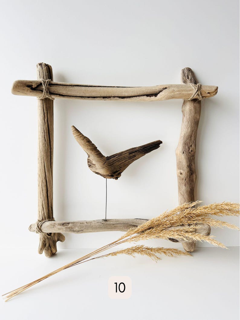May include: A rustic wooden frame with a driftwood sculpture and dried wheat stalks. The frame is constructed from weathered wood pieces tied together with twine. The sculpture resembles a bird in flight. The number 10 is in the lower right corner.