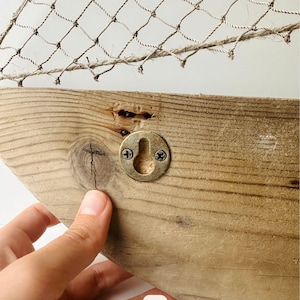 May include: A rustic wooden wall decor piece with a fishnet design. The wooden base is light brown with a metal hook for hanging. The fishnet is made of a natural fiber.
