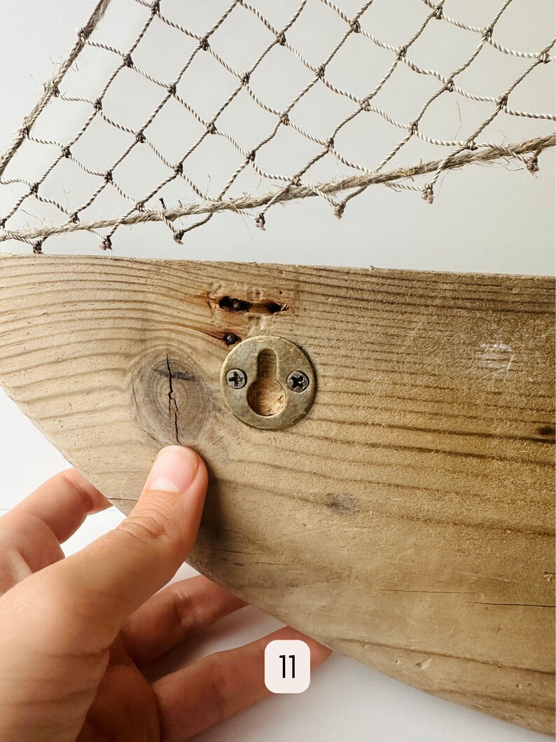 May include: A rustic wooden wall decor piece with a fishnet design. The wooden base is light brown with a metal hook for hanging. The fishnet is made of a natural fiber.