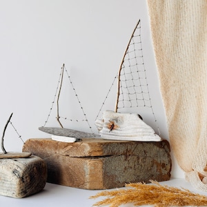 Puede incluir: Tres esculturas decorativas de veleros de madera. Los barcos est&aacute;n hechos de madera flotante y peque&ntilde;os bloques de madera. Las velas est&aacute;n hechas de malla de alambre y ramitas. Los barcos se exhiben sobre un bloque de madera y una superficie blanca.