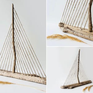 Puede incluir: Escultura r&uacute;stica de velero de madera flotante. El barco presenta una base y un m&aacute;stil de madera, con aparejo de cuerda que forma la vela. Los tonos naturales de la madera se complementan con el fondo neutro y los acentos de hierba seca.
