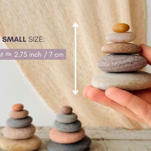May include: A stack of five smooth, rounded stones in varying shades of tan, gray, and brown. The text SMALL SIZE: Height &asymp; 2,75 inch is visible. The stones are arranged in a pyramid shape, with the smallest amber-colored stone at the top.