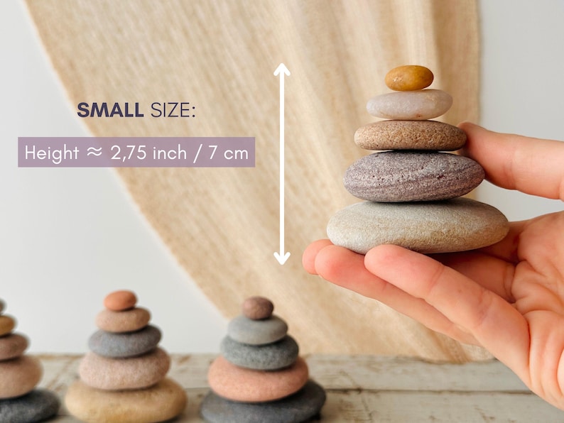 May include: A stack of five smooth, rounded stones in varying shades of tan, gray, and brown. The text SMALL SIZE: Height &asymp; 2,75 inch is visible. The stones are arranged in a pyramid shape, with the smallest amber-colored stone at the top.