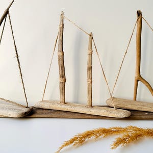 Puede incluir: Esculturas de veleros de madera flotante. Las piezas de arte r&uacute;sticas presentan bases y m&aacute;stiles de madera, con aparejo de cuerda. Los tonos de madera natural y el dise&ntilde;o sencillo crean un tema costero o n&aacute;utico. Los veleros est&aacute;n dispuestos sobre una base de madera.