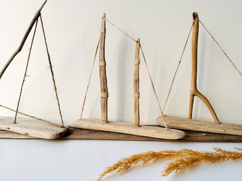 Puede incluir: Esculturas de veleros de madera flotante. Las piezas de arte r&uacute;sticas presentan bases y m&aacute;stiles de madera, con aparejo de cuerda. Los tonos de madera natural y el dise&ntilde;o sencillo crean un tema costero o n&aacute;utico. Los veleros est&aacute;n dispuestos sobre una base de madera.