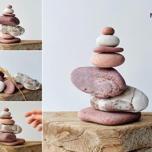 Puede incluir: Una pila de piedras lisas, rosadas y blancas, equilibradas unas sobre otras. Las piedras est&aacute;n dispuestas en forma de pir&aacute;mide y se encuentran sobre un trozo de madera desgastada. El texto "N-51" es visible en la esquina superior derecha de la imagen.