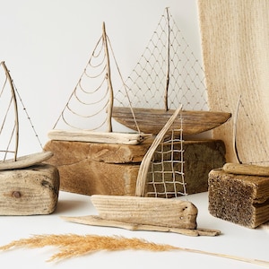 Puede incluir: Una colecci&oacute;n de veleros de madera flotante hechos a mano. Cada barco presenta un casco de madera y una vela hecha de materiales naturales. Los barcos se exhiben sobre bloques de madera y una superficie texturizada, creando un tema n&aacute;utico r&uacute;stico.