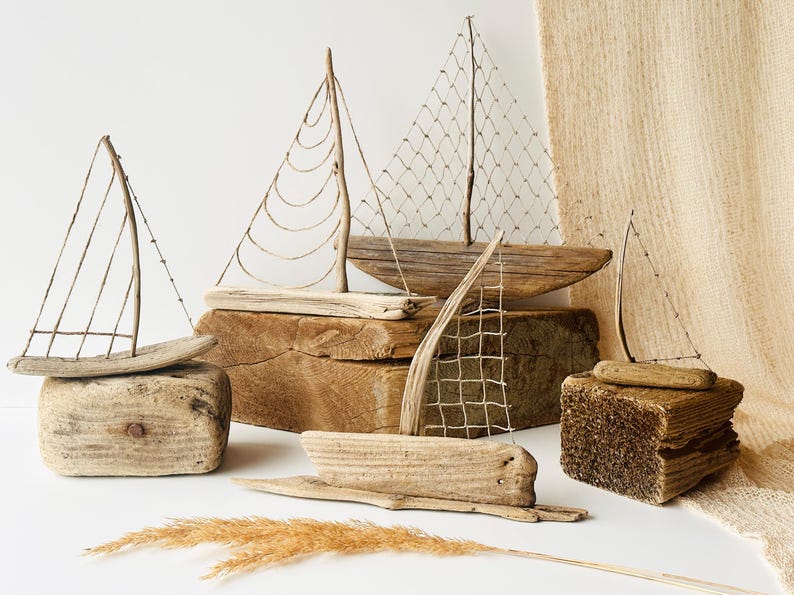 Puede incluir: Una colecci&oacute;n de veleros de madera flotante hechos a mano. Cada barco presenta un casco de madera y una vela hecha de materiales naturales. Los barcos se exhiben sobre bloques de madera y una superficie texturizada, creando un tema n&aacute;utico r&uacute;stico.