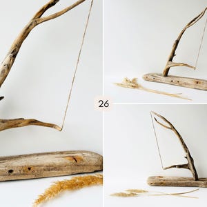 Puede incluir: Escultura de madera flotante con una base marr&oacute;n claro y una rama curvada. Una fina cuerda cuelga de la rama. El n&uacute;mero "26" es visible. Se colocan hierbas secas cerca de la base. Escultura de madera natural.