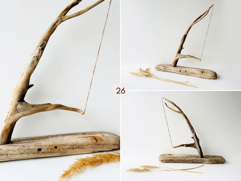 Puede incluir: Escultura de madera flotante con una base marr&oacute;n claro y una rama curvada. Una fina cuerda cuelga de la rama. El n&uacute;mero "26" es visible. Se colocan hierbas secas cerca de la base. Escultura de madera natural.