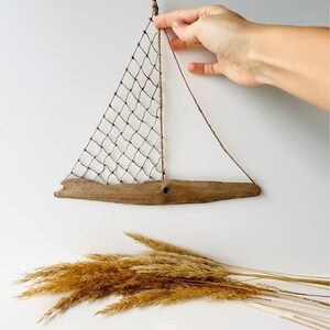 Close up of rustic driftwood sailboat wall decor showing net sail and rope details, beach house nautical art held by hand for size reference