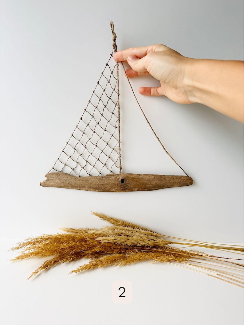 Close up of rustic driftwood sailboat wall decor showing net sail and rope details, beach house nautical art held by hand for size reference