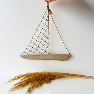 May include: A handcrafted sailboat decoration made from natural materials. The boat features a wooden hull, a net sail, and twine rigging. The image also includes a bundle of dried, golden-brown ornamental grass, and the number 6.