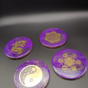 Pode incluir: Quatro  tapetes redondos roxos com glitter dourado e desenhos geométricos dourados. Os desenhos incluem um dragão, uma flor da vida, um símbolo yin yang e um padrão geométrico.