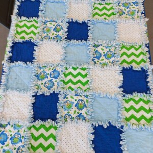 May include: A blue and green baby quilt with a patchwork design featuring owls, zigzags, and polka dots. The quilt is made with soft, cuddly fabric and is perfect for a baby's nursery.
